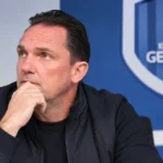 Een KRC Genk-staflid in donkere clubkleding tijdens een intern overleg in een vergaderruimte.