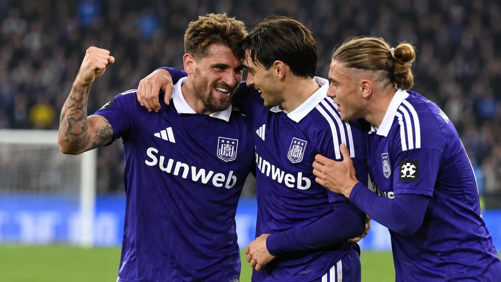 Een groep voetballers in paarse wedstrijdshirts viert samen op het veld.