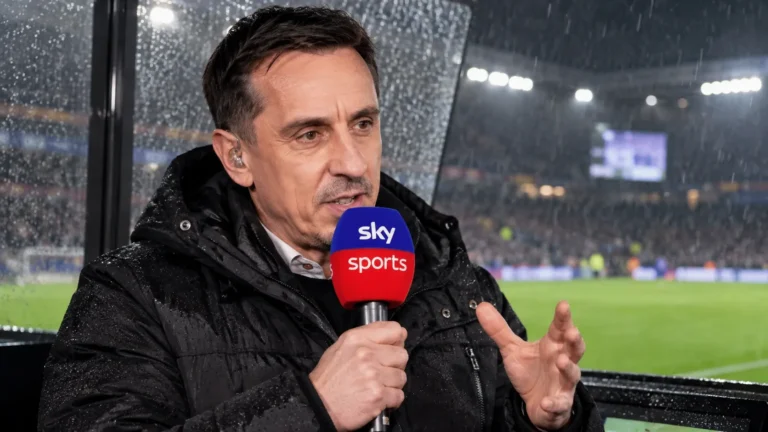Gary Neville spreekt met een microfoon aan een overdekte commentaarpositie bij een regenachtig stadion.