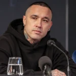 Radja Nainggolan zit in een zwarte hoodie aan een perstafel met microfoons.