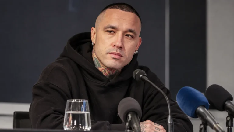 Radja Nainggolan zit in een zwarte hoodie aan een perstafel met microfoons.