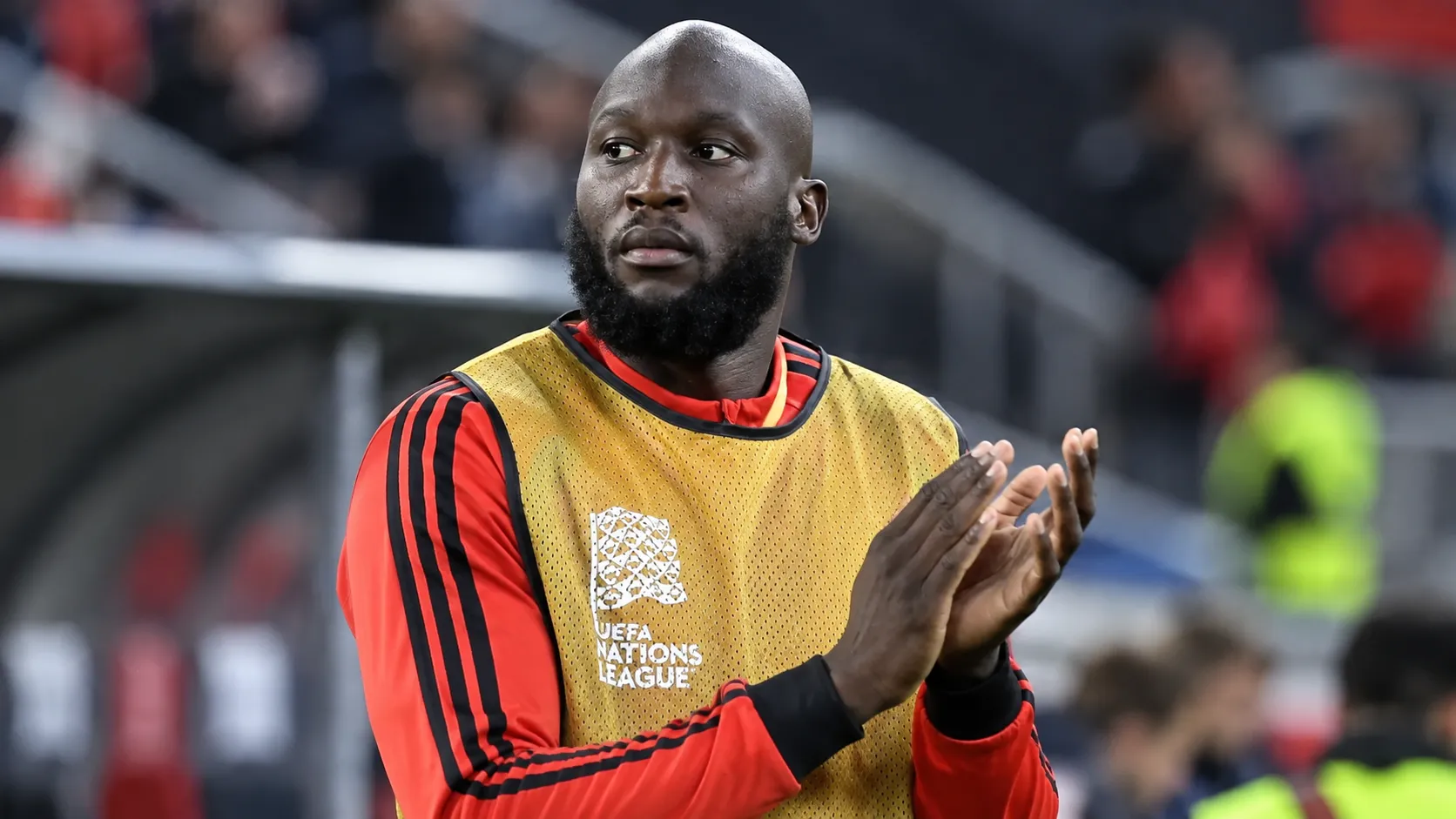 Romelu Lukaku in Belgisch trainingsshirt en geel hesje aan de zijlijn.