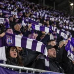 Een collectieve groep Anderlecht-supporters met paars-witte sjaals in de tribune.