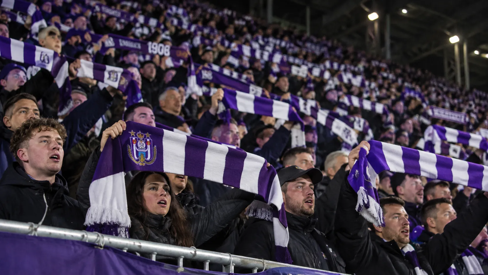 Een collectieve groep Anderlecht-supporters met paars-witte sjaals in de tribune.
