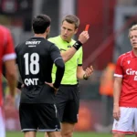 Een scheidsrechter spreekt met spelers tijdens een onderbreking in een wedstrijd van Standard.
