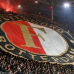 Een volle Feyenoord-tribune met supporters onder een groot clubspandoek.
