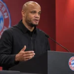 Vincent Kompany spreekt op een persmoment van Bayern München achter een spreekgestoelte.