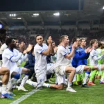 Een groep KAA Gent-spelers in wit-blauwe tenues groet samen langs de zijlijn.