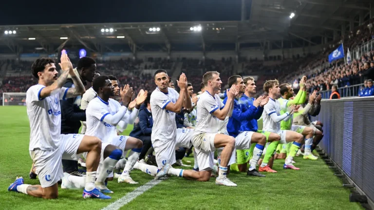 Een groep KAA Gent-spelers in wit-blauwe tenues groet samen langs de zijlijn.