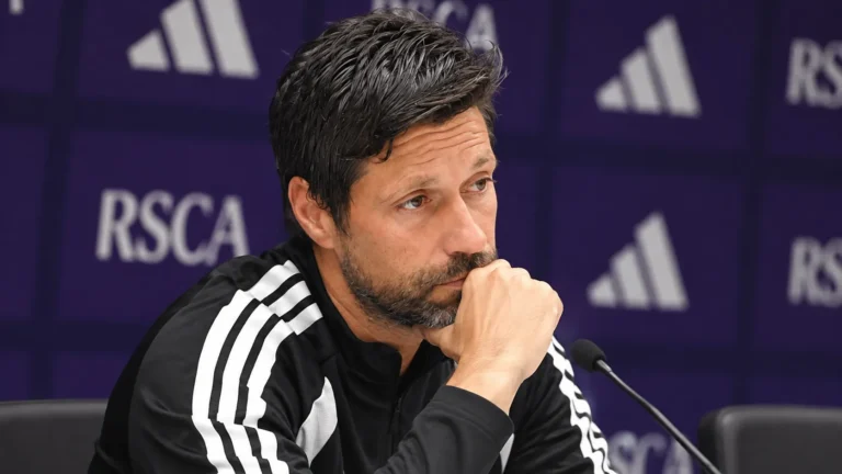 Een staflid van RSC Anderlecht tijdens een persmoment in een paarse persruimte.