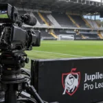 Een vaste televisiecamera naast het veld met een Jupiler Pro League-bord op de achtergrond.