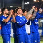Een groep KAA Gent-spelers in blauwe shirts viert samen langs het veld.