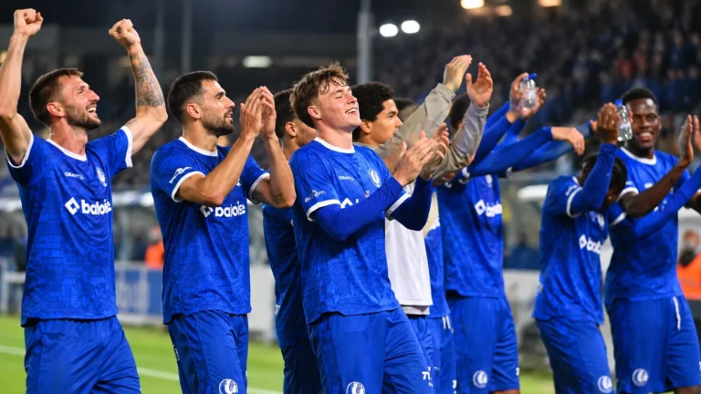Een groep KAA Gent-spelers in blauwe shirts viert samen langs het veld.