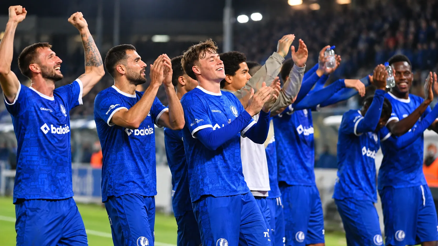 Een groep KAA Gent-spelers in blauwe shirts viert samen langs het veld.