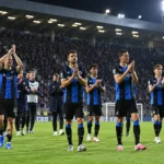 Club Brugge-spelers applaudisseren samen op het veld onder stadionverlichting.