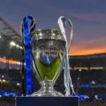 De Champions League-trofee op een sokkel in een stadion bij avondlicht.