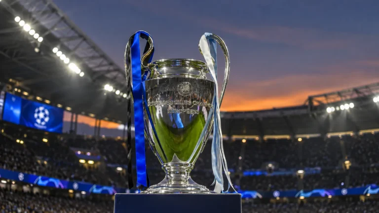 De Champions League-trofee op een sokkel in een stadion bij avondlicht.
