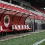Lege technische zone van Royal Antwerp FC met het clubembleem op de rugwand van de dug-out.