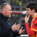 Een speler van KV Mechelen praat na de wedstrijd met een coach langs de zijlijn.