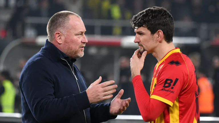 Een speler van KV Mechelen praat na de wedstrijd met een coach langs de zijlijn.