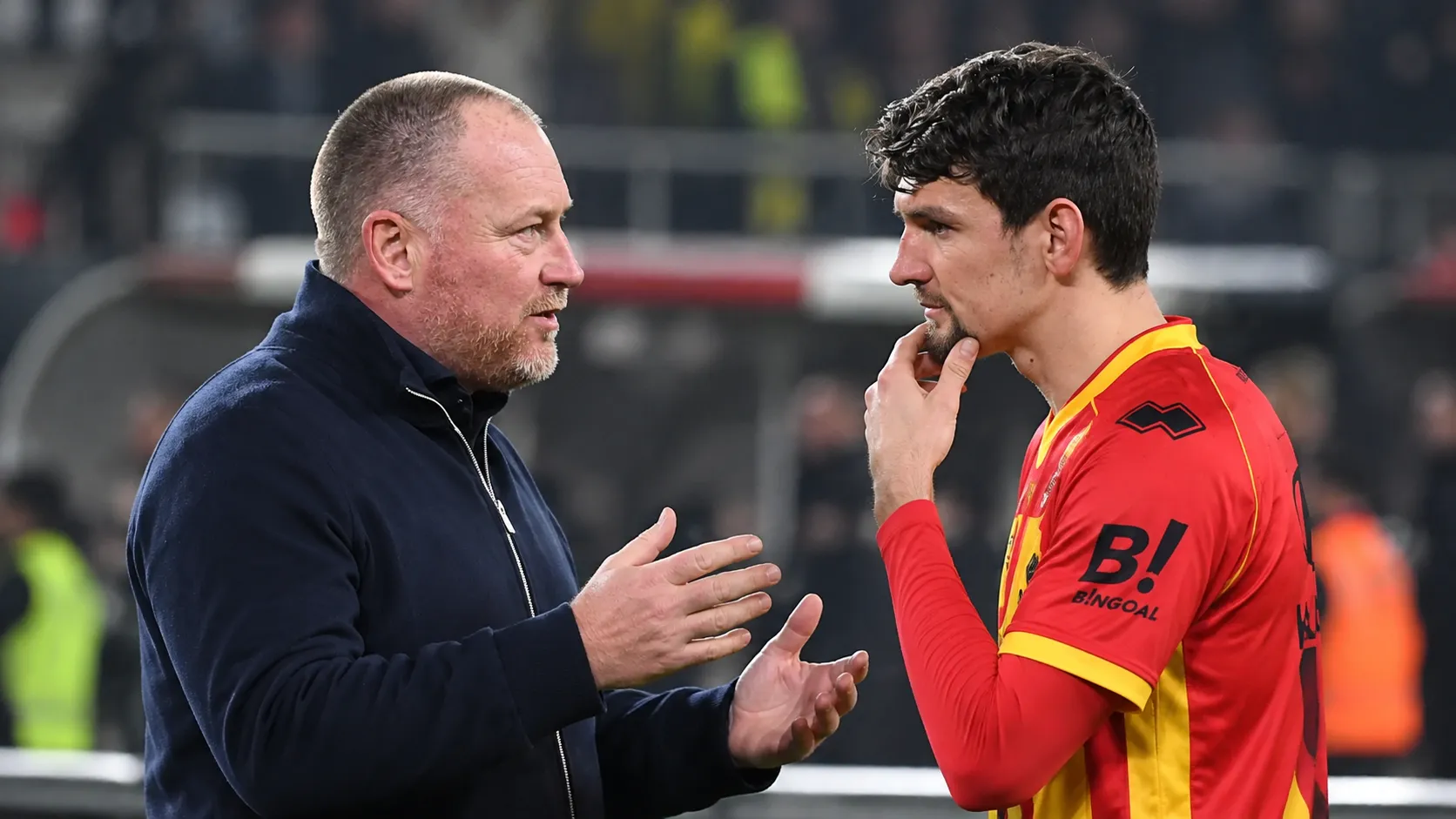 Een speler van KV Mechelen praat na de wedstrijd met een coach langs de zijlijn.