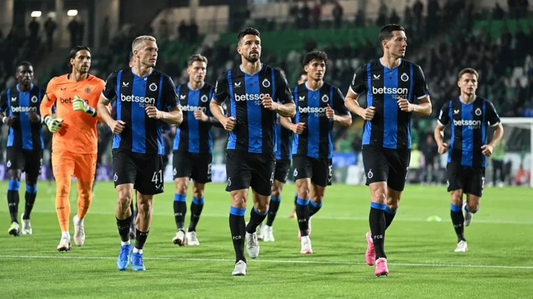 Een groep spelers van Club Brugge warmt samen op onder stadionlichten.