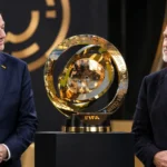 Twee voetbalofficials naast de gouden trofee van het WK voor clubs.