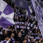 Een groep Anderlecht-supporters zwaait met paars-witte vlaggen en houdt sjaals omhoog op de tribune.