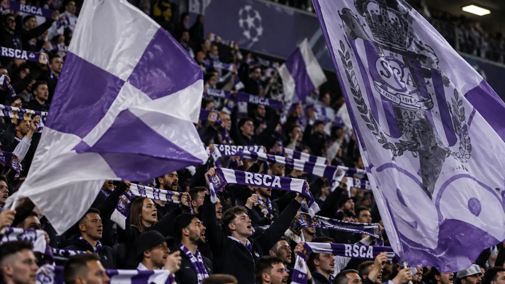 Een groep Anderlecht-supporters zwaait met paars-witte vlaggen en houdt sjaals omhoog op de tribune.