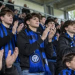Een collectieve groep Internazionale-supporters applaudisseert met blauw-zwarte sjaals in de tribune.