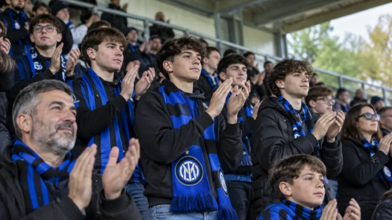 Een collectieve groep Internazionale-supporters applaudisseert met blauw-zwarte sjaals in de tribune.