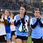 Een groep voetbalsters applaudisseert na een wedstrijd langs het veld.