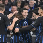 Een groep spelers in zwart-blauwe tenues viert samen voor de tribune.