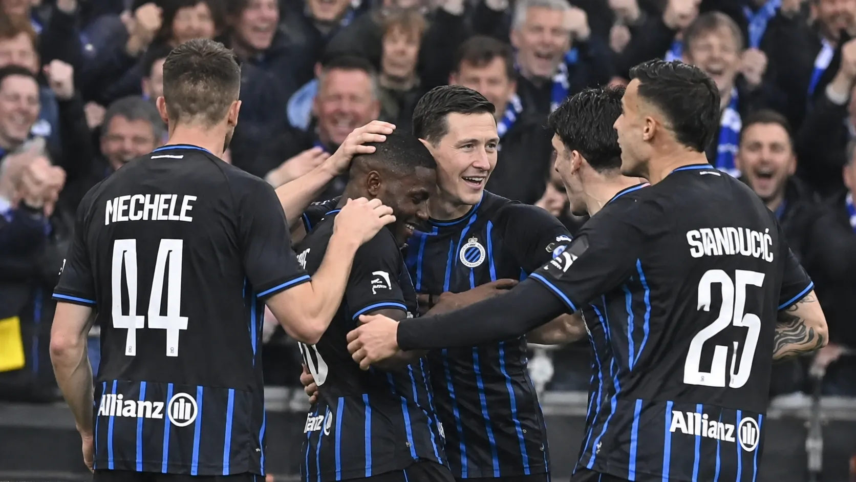 Een groep spelers in zwart-blauwe tenues viert samen voor de tribune.