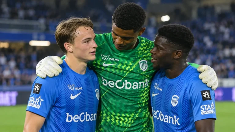 Drie spelers van KRC Genk steunen elkaar na een wedstrijd aan de rand van het veld.