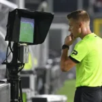 Een scheidsrechter bij een VAR-monitor langs het voetbalveld.