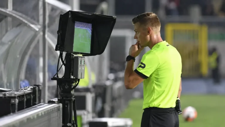 Een scheidsrechter bij een VAR-monitor langs het voetbalveld.