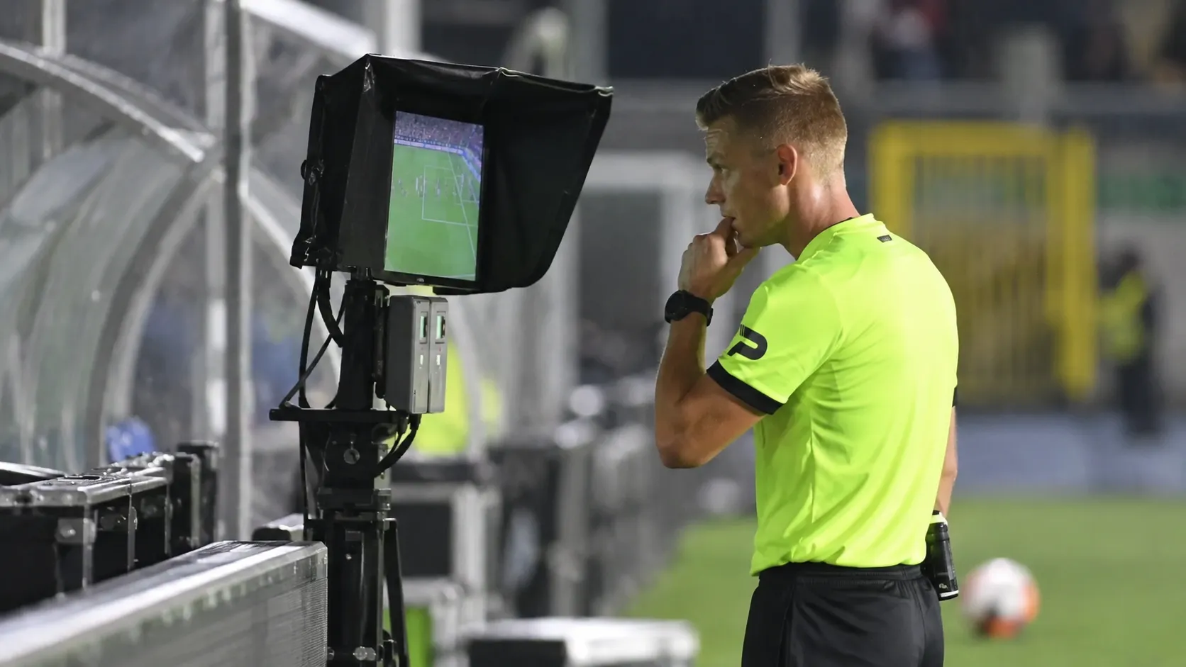 Een scheidsrechter bij een VAR-monitor langs het voetbalveld.