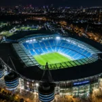 Verlicht Manchester City-stadion gezien vanuit de lucht bij nacht.