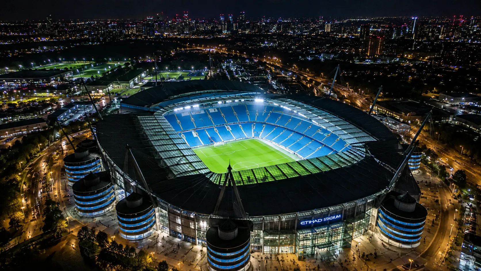 Verlicht Manchester City-stadion gezien vanuit de lucht bij nacht.