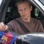 Frenkie de Jong zit in een auto en signeert een Barcelona-shirt bij het geopende raam.