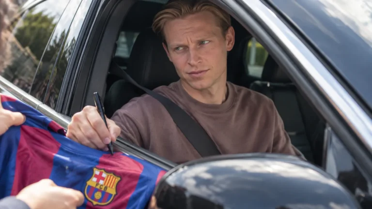 Frenkie de Jong zit in een auto en signeert een Barcelona-shirt bij het geopende raam.