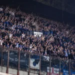 Een volle groep blauw-zwarte supporters applaudisseert in een stadiontribune.