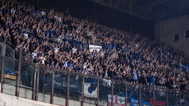 Een volle groep blauw-zwarte supporters applaudisseert in een stadiontribune.