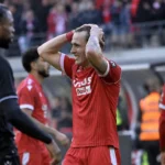 Spelers in rode en zwarte wedstrijdtenues tijdens een gespannen moment na afloop van een derby.