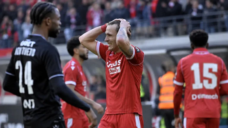 Spelers in rode en zwarte wedstrijdtenues tijdens een gespannen moment na afloop van een derby.