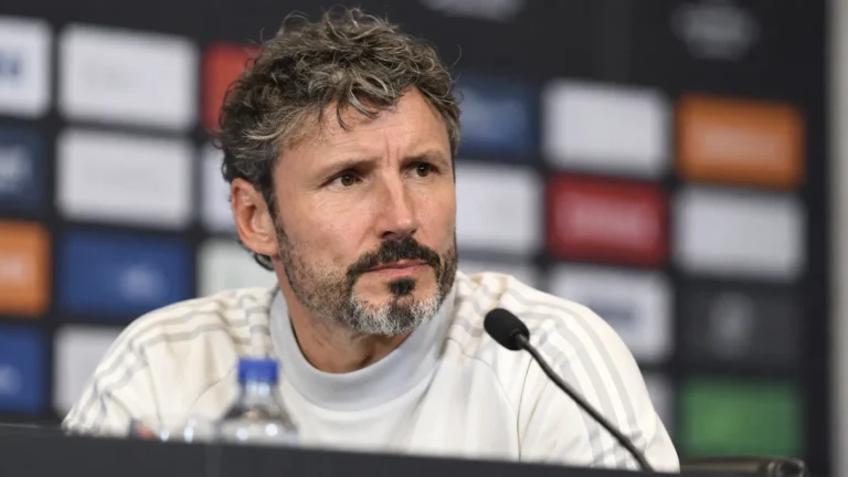 Een voetbalcoach spreekt tijdens een persconferentie.