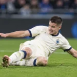 Een Club Brugge-speler in een licht wedstrijdtenue ligt op het gras tijdens een wedstrijd.