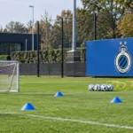 Leeg jeugdtrainingsveld van Club Brugge met een blauw clubbord langs de zijlijn.