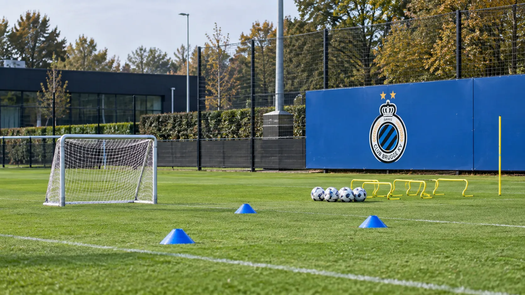 Leeg jeugdtrainingsveld van Club Brugge met een blauw clubbord langs de zijlijn.
